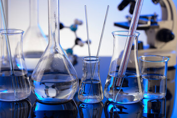 Coronavirus pandemic theme. Science research concerning fast covid tests and anti-covid vaccine. Microscope, beakers and test tubes on blue background.