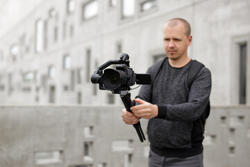 filmmaking, hobby and creativity concept - videographer shooting video using modern dslr camera on 3-axis gimbal over concrete building. Focus on camera