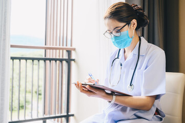 Asian healthcare worker reading patient medical history about diagnosis and prescriptions. Female therapeutist working alone in hospital office doing paperwork.