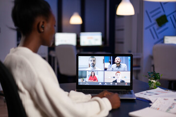 African employee working overtime from business office late at night discussing with partners online using webcam. Diverse team talking during corporate meeting using technology network wireless.