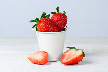 Whole and sliced ripe strawberries in a small bucket on a white wooden table. 