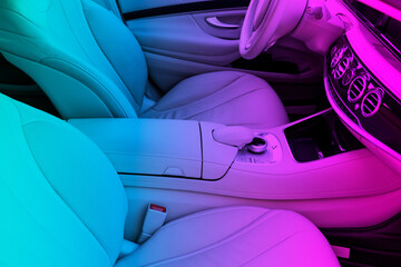 White leather interior of the luxury modern car in blue and pink lights. Leather comfortable white seats and multimedia. Steering wheel and dashboard. Automatic gear shift. Car interior details