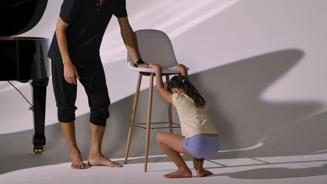 Personal ballet lesson for little girl. Professional teacher teaches child elements of dance and corrects positioning legs and stretching. Diligent ballet student trains on white studio background.