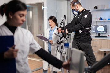 Man athlete running witjh biomechanics attached to his body and mask. Physician looking at notes...
