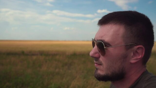 Portrait of a Young Man in Sunglasses on the Background of a Wheat Field and Blue Sky.
