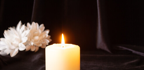 A burning candle and white flower on a black background. The concept of condolences, mourning, and funerals.