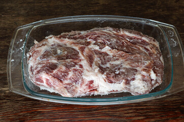 Homemade Capicola (coppa). Dry-cured pork loin step-by-step recipe. Large Whole piece of raw pork meat in glass container after three days of salting. Pickled neck. Traditional Italian cuisine.