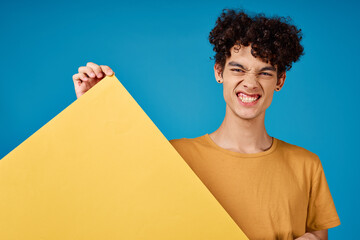 Cheerful guy with curly hair of yellow asters in his hands studio blue background