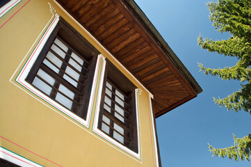 Attractive view upwards of traditional Bulgarian house exterior with orange painted walls, wooden windows and eaves of the roof, blue sky. Architecture style from Bulgarian National Revival period.
