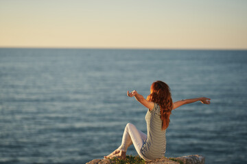 happy woman in a t-shirt and trousers by the sea raised her hands up