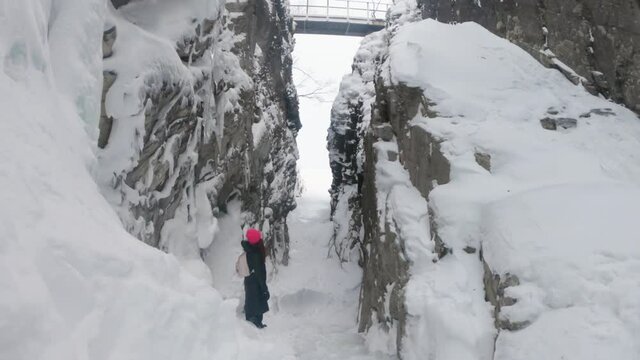 Girl standing in a big rocky cave in Björkliden, Sweden. Frozen waterfall and a lot of snow around her.