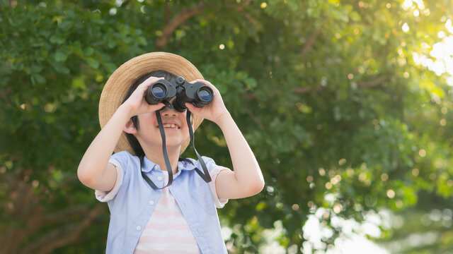 Cute asian child looks in binoculars outdoors in sunny summer day
