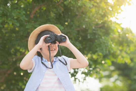 Cute asian child looks in binoculars outdoors in sunny summer day