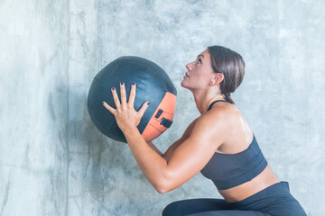 A beautiful female athlete throws a medicine ball at the wall during training at a gym