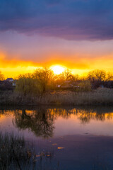 Beautiful golden sunset with reflection of clouds in the lake in the village panorama