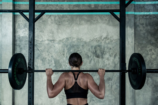 A beautiful female athlete prepares to do a barbell back squat at a gym 