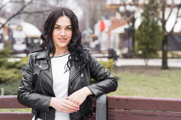 Beautiful brunette woman with curly hair posing outdoors while sitting on a bench