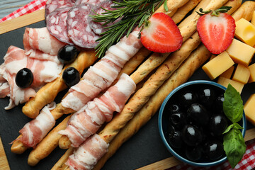 Tasty grissini sticks with bacon and snacks, close up