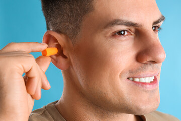 Man inserting foam ear plug on light blue background, closeup