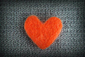 A red heart made of wool lies on a gray knitted background.The concept of handwork, needlework and needlework.Background for Valentine's Day, Birthday, Mother's Day.Top view.Flat styling style