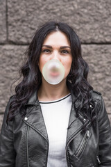 Beautiful brunette woman with curly hair inflates a bubble gum ball on the street