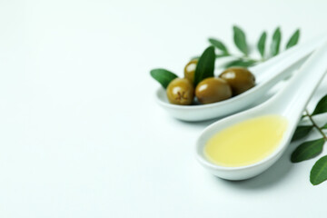Spoons with olives and oil, and twigs on white background