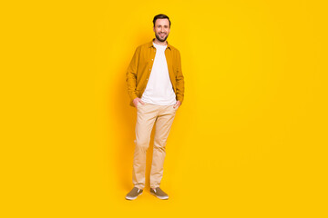 Full length photo of charming cute young guy wear casual clothes smiling standing arms pockets isolated yellow color background