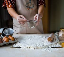 Hands of a girl on a wooden table in an apron knead the dough. Around the flour, eggs, salt.