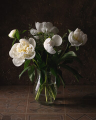 A bouquet of white peonies in a glass jug on a dark background