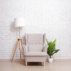 Armchair, lamp and plant over brick wall