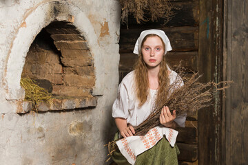 Natural Portrait of Sensual Caucasian Redhaired Girl in Rustic Style Dress Posing With Heather Bouquet in Old House In Front Of the Stove.