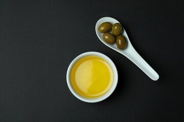 Spoon with olives and bowl of oil on black background