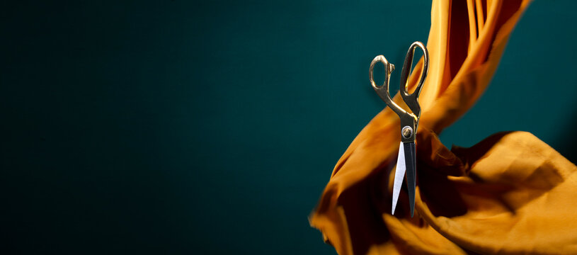 Tailor cissors against wavy yellow satin, dark green background.Empty space for design