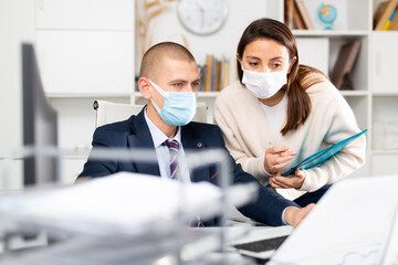 Corporate business coleagues businessman and businesswoman in face masks discussing something and working together in modern office