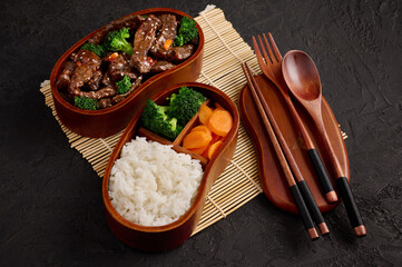 Healthy balanced lunch box. Beef and brocolli stir fry with side of rice and carrots on dark...