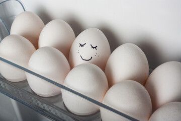 smiling egg in a row of white eggs in the fridge