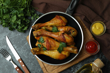 Concept of delicious eating with pan of roast chicken drumsticks on black smokey table