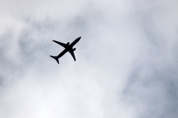Silhouette of airplane flying in blue sky with white clouds. Passenger plane at flight, travel concept