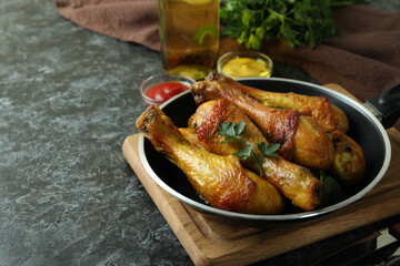 Concept of delicious eating with pan of roast chicken drumsticks on black smokey table