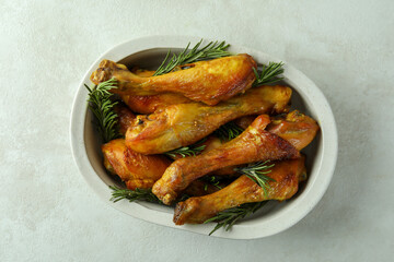 Baking tray with roast chicken drumsticks on white textured background