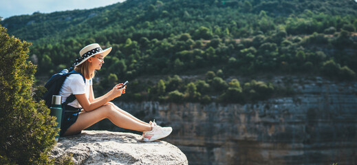 hipster traveler in hat and backpack ralaxing in nature and using internet on smartphone, tourist...