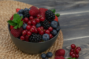Ripe sweet different berries in bowl on wooden table. Harvest Concept.