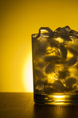 Glass of alcohol with ice on wooden table yellow background front view copy space