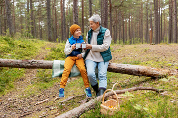 picking season, leisure and people concept - grandmother and grandson having picnic and drinking...