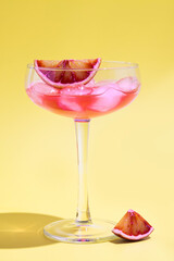 Party pink juice cocktail and ice with red oranges in glass on yellow background. Summer drinks. Close up