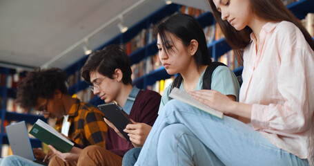 Multi-ethnic group of students sitting on floor in library studying