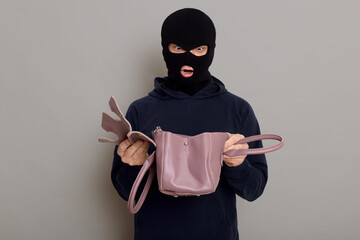 Young male criminal with stolen bag in his hands, looks in inside with shocked expression on his...