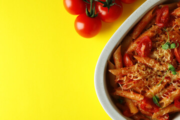 Tray with pasta with tomato sauce and ingredients on yellow background, top view