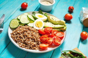 Vegan lunch bowl with avocado, egg, cucumber, tomato and buckwheat on blue wooden background