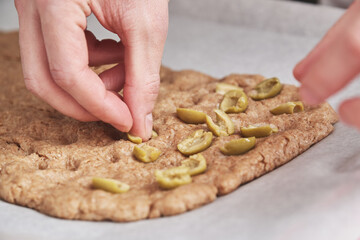 Unrecognizable young caucasian man putting olives on a dough. He is making focaccia.
